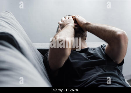 Premuto l Uomo sdraiato sul divano e sofferenza tenendo le mani sul viso Foto Stock