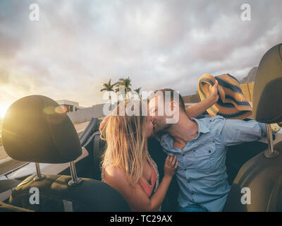 Felice coppia giovane avente baciare in autovettura convertibile durante il loro viaggio su strada - alla moda gli amanti della romantica avente un momento di gara in cabriolet auto Foto Stock