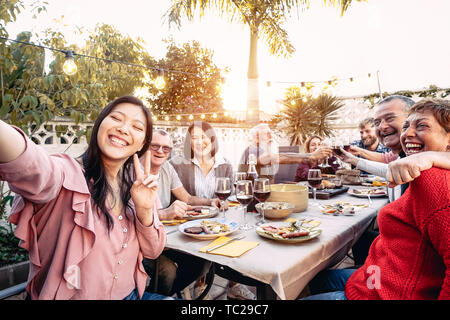 La famiglia felice il tifo e tostatura con red bicchieri di vino a cena outdoor - Persone con differenti età e di etnia divertendosi al barbecue party Foto Stock