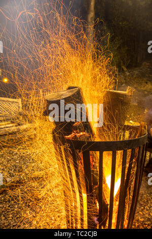 Un fuoco che brucia pit cestello in acciaio nelle tenebre fredda notte di ottobre in autunno con il fuoco scintille galleggianti intorno Foto Stock