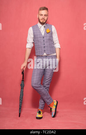Un giovane gentiluomo, ponendo in studio, indossare abiti formali suit, con un ombrello. shot su sfondo rosa. Foto Stock