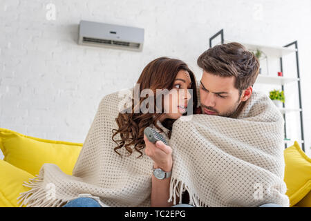 Congelati matura il riscaldamento sotto coperta mentre è seduto sul divano sotto il condizionatore d'aria di casa Foto Stock