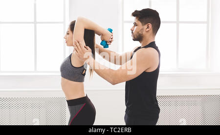 L'uomo trainer aiutando ragazza sportivo facendo esercizio con bumbbell Foto Stock