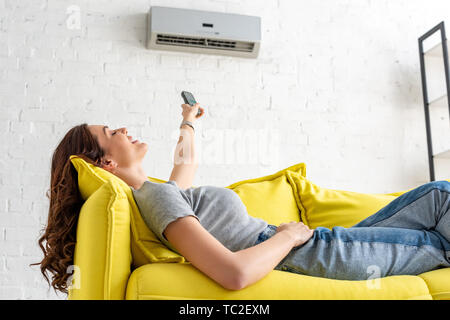 Attraente ragazza rilassante sotto il condizionatore d'aria e tenendo premuto Comando remoto Foto Stock