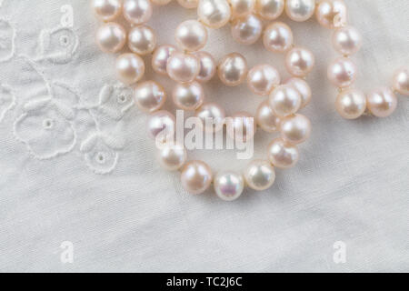 Collana di perle su bianco lino ricamato sullo sfondo - vista superiore foto di vere perle rosa Foto Stock