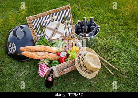 In stile vintage vimini cesto da picnic con un assortimento di verdure fresche per insalate e croccanti baguette francesi al fianco di un raffreddatore di argento con bottiglia Foto Stock