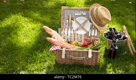 Cesto picnic riempito con diversi prodotti alimentari tra cui baguette e verdure accanto alla benna di bottiglie Foto Stock