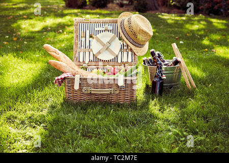 Vimini cesto da picnic con insalata vegetariana ingredienti, uve e baguette francesi al fianco di un argento wine cooler con bottiglie di birra in un vintage s Foto Stock