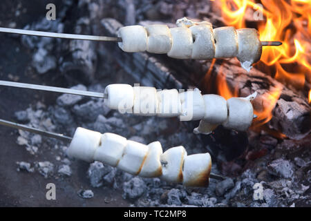 Tre spiedini di fusione sfrigolanti white marshmallows la tostatura su un fuoco sopra la brace a un barbecue estivo Foto Stock
