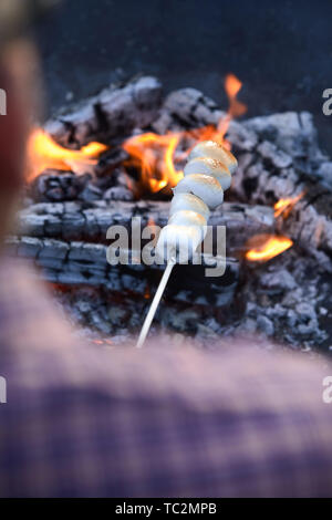L'uomo la tostatura uno spiedino di marshmallows alla brace di un fuoco caldo in un sopra la spalla vista della caramella Foto Stock