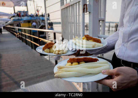 Berlino, Germania. 04 Giugno, 2019. Un cameriere porta un piatto di asparagi alla MS Havel Regina prima di partire per il Seeheimer Kreis asparagi crociera sul Lago Wannsee. Il Seeheimer Kreis, un gruppo di lavoro del DOCUP i deputati del Parlamento europeo, ha organizzato il viaggio di asparagi dal 1961. Credito: Christoph Soeder/dpa/Alamy Live News Foto Stock