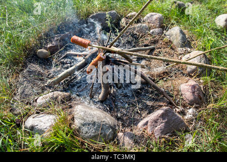 Saporite salsicce gocciolamento con lardo cotto su un fuoco aperto. Un camino in un giardino di casa. Stagione della primavera. Foto Stock