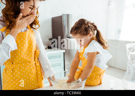 Scioccato madre guardando la figlia di mettere le mani nella ciotola con la farina Foto Stock