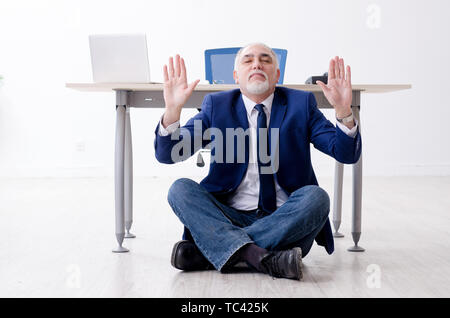 Imprenditore invecchiato facendo esercizi yoga in ufficio Foto Stock