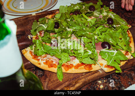 Gustosa gustosa pizza con formaggio, pomodori, rucola, olive, basilico sul tavolo di legno Foto Stock
