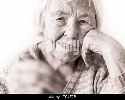 Triste anziani donna seduta al tavolo a casa e guardando miseramente solo al restante moneta dalla pensione nella sua mano. Foto Stock