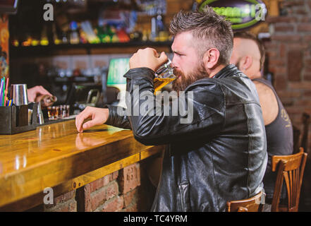 Ordine di bere alcol. Il bar è un luogo rilassante hanno bere e rilassarsi. Uomo con barba trascorrere il tempo libero nella barra di colore scuro. Hipster rilassante presso il bar con birra. Brutale parigamba uomo barbuto sedersi al banco bar bere birra. Foto Stock
