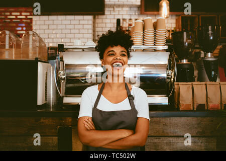 Donna barista all'interno di lei coffee shop. Donna barista nel buon umore in piedi di fronte sul contatore. Foto Stock