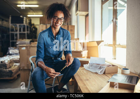 Sorridente giovane donna seduta al suo posto di lavoro. Fiducioso online business owner guardando la fotocamera e sorridente. Foto Stock