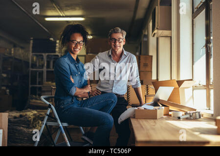 Ritratto di un uomo e di una donna in piedi nel negozio online di magazzino. Business Partner insieme guardando la fotocamera e sorridente. Foto Stock