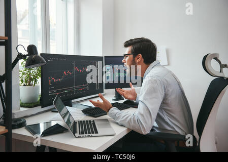 Alcun modo scioccato giovane imprenditore o commerciante nel convenzionale sta gridando e gesticolando mentre guardando al trading grafici e dati finanziari in ufficio. Stock Exchange. Il trading finanziario concetto. Concetto di investimento. Mercato Forex Foto Stock