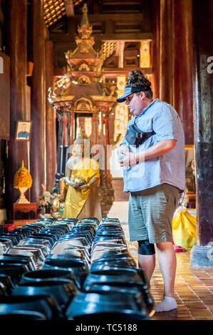 Un turista fa cadere monete nelle ciotole come una donazione nel Tempio di Wat Phant Tao, Chiang mai, Thailandia. Foto Stock