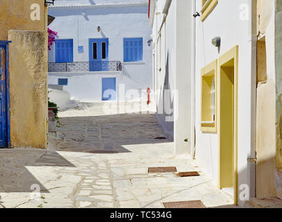 Bella tranquilla lastricata in pietra vicolo vuoto, case bianche con il blu e il giallo di windows a mezzogiorno tempo e idrante di fuoco Tinos Island, Grecia. Foto Stock