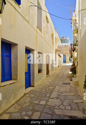 Bella tranquilla lastricata in pietra vicolo vuoto con case bianche con finestre blu a mezzogiorno tempo, isola di Tinos, Grecia. Foto Stock