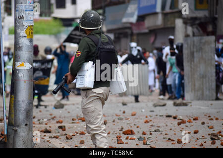 Un poliziotto indiano sorge sulla protezione come contestatori del Kashmir getta pietre durante gli scontri a Srinagar. Le forze indiane in Srinagar usato gas lacrimogeni fumogeni e proiettili per disperdere centinaia di manifestanti che hanno preso a strade dopo Eid-ul-Fitr preghiere per protestare contro la regola di indiana nella regione. Foto Stock