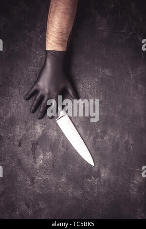 Mani maschio nero con guanti in lattice e coltello su sfondo scuro Foto Stock