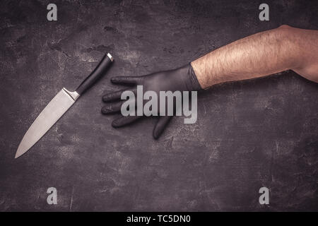 Grande coltello e mani maschio nero con guanti in lattice su sfondo scuro Foto Stock