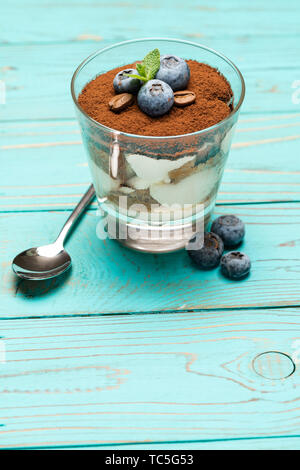 Tiramisù classico dessert in un bicchiere con mirtilli blu su sfondo di legno Foto Stock