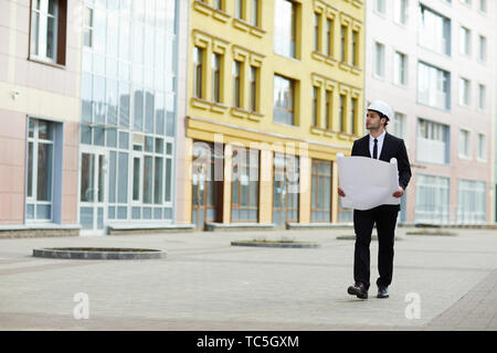 A piena lunghezza Ritratto di bello imprenditore mediorientale indossando hardhat camminando verso la telecamera al sito in costruzione, spazio di copia Foto Stock