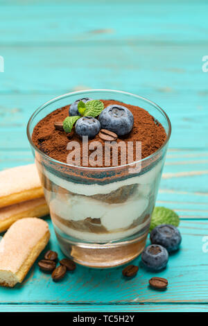 Tiramisù classico dessert in un bicchiere con mirtilli blu su sfondo di legno Foto Stock