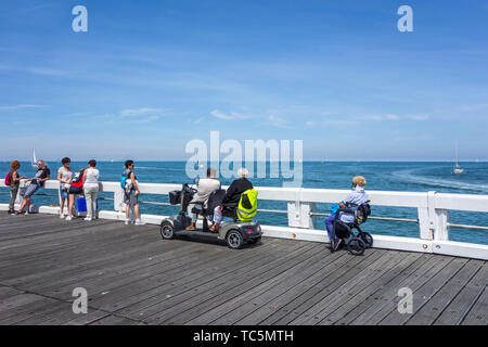 Donna disabile in carrozzina e per persone handicappate in duo due persona scooter di mobilità a guardare le barche a vela in mare dal jetty Foto Stock