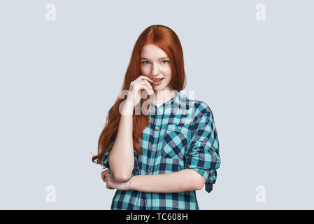 Ritratto di affascinante redhead femmina sensualmente sorridente, guardando la fotocamera con curiosità e interesse su sfondo grigio Foto Stock