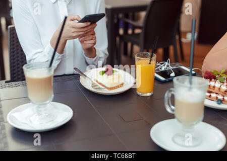 Le mani delle donne rendendo la foto del dolce con il telefono cellulare mentre sedendo nel confortevole ristorante Foto Stock