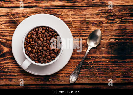 Chicchi di caffè tostati in bianco cup oltre rustico superficie in legno Foto Stock