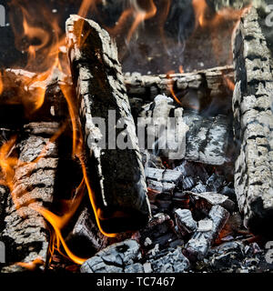 Carboni Ardenti e masterizzazione carbonizzati ciocchi di legna con leccamento fiamme arancione ai lati in un incendio in un vicino in piena vista del telaio Foto Stock