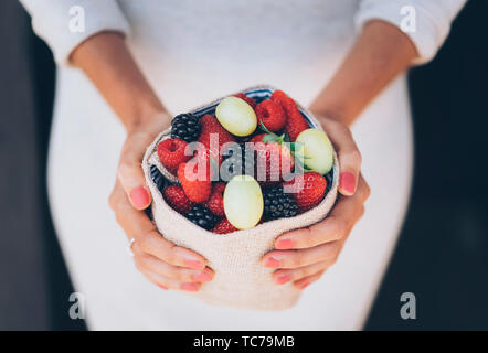 Una sana e succosa e frutti di bosco con la donna con le mani abito bianco Foto Stock