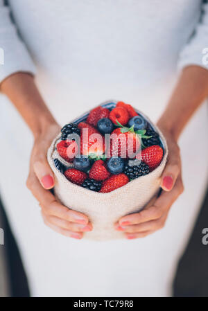 Una sana e succosa e frutti di bosco con la donna con le mani abito bianco Foto Stock