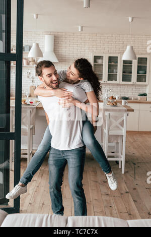 Ridendo uomo barbuto che trasportano ragazza sovrapponibile in cucina Foto Stock