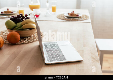 Laptop e ciotola con frutta fresca sul tavolo in cucina Foto Stock