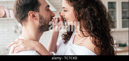 Panoramica di sorridere amare giovane in bianche vesti abbracciando in cucina Foto Stock