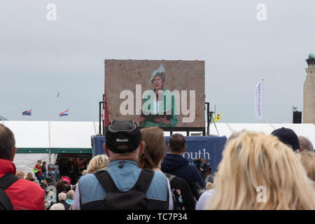 Una folla guardando il grande schermo come Theresa Maggio il primo ministro del Regno Unito dà un discorso durante il D-Day 75 commemorazioni in Portsmouth Foto Stock