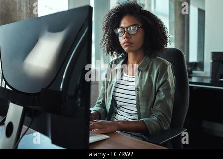 Giovane imprenditrice africana la digitazione sulla tastiera di PC desktop Foto Stock