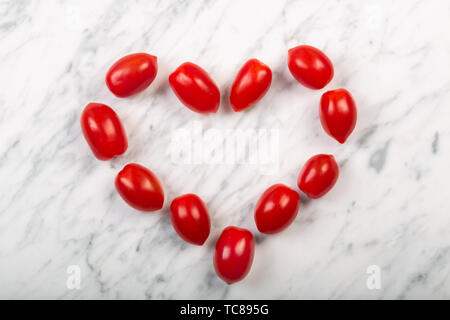 Pomodori ciliegia stabiliti a forma di cuore su un marmo bianco di sfondo, vista dall'alto Foto Stock