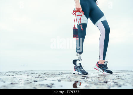 Facendo del mio meglio. Immagine ritagliata della donna disabile in abbigliamento sportivo con gamba protesico holding corda da salto in piedi di fronte al mare. Sportivo disabili. Uno stile di vita sano. Cardio Foto Stock