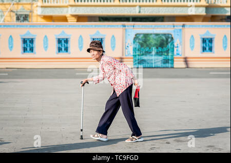 Una vecchia signora cambogiana fa il suo modo attraverso la strada di fronte al Grand Palace, Phnom Penh Cambogia del Sud Est Asiatico. Foto Stock