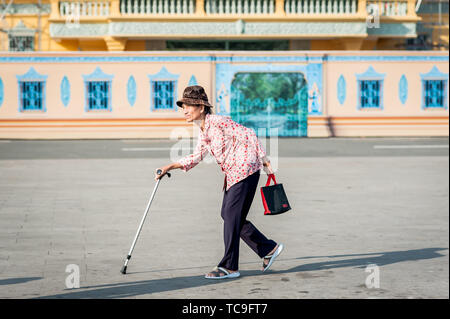 Una vecchia signora cambogiana fa il suo modo attraverso la strada di fronte al Grand Palace, Phnom Penh Cambogia del Sud Est Asiatico. Foto Stock